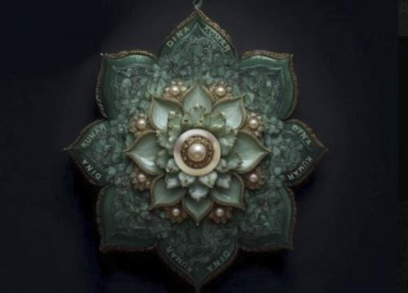 The image shows a green and white flower-shaped ornament, possibly a pendant, with the text 'Dina Kumar' inscribed on its petals, set against a dark background.