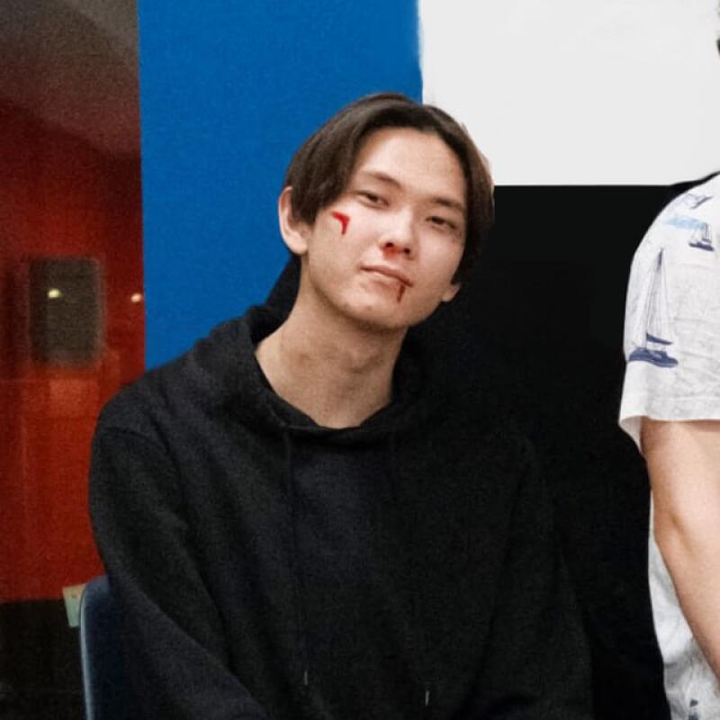 A young person with fake blood on their face and wearing a black hoodie poses in front of a colorful backdrop.