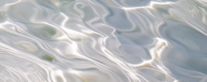 The image shows the surface of water with light reflecting off its ripples, creating an abstract, flowing pattern of whites and grays.