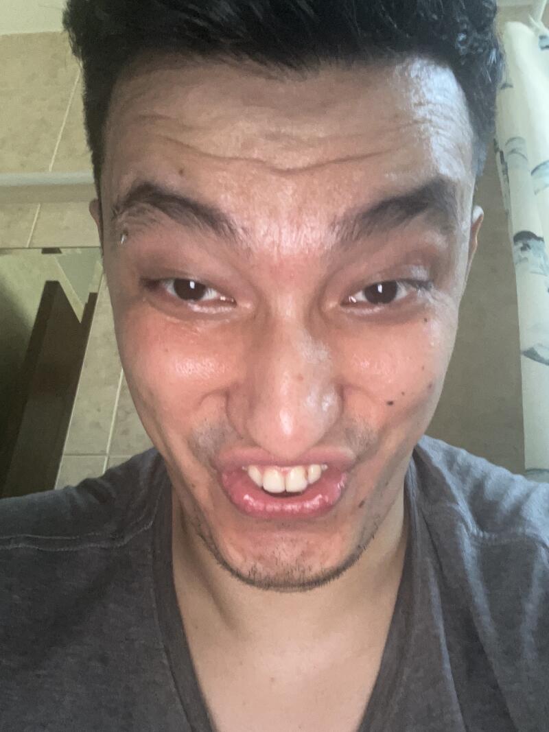 A man with an eyebrow piercing is smiling widely, showing his teeth and wrinkles on his forehead.