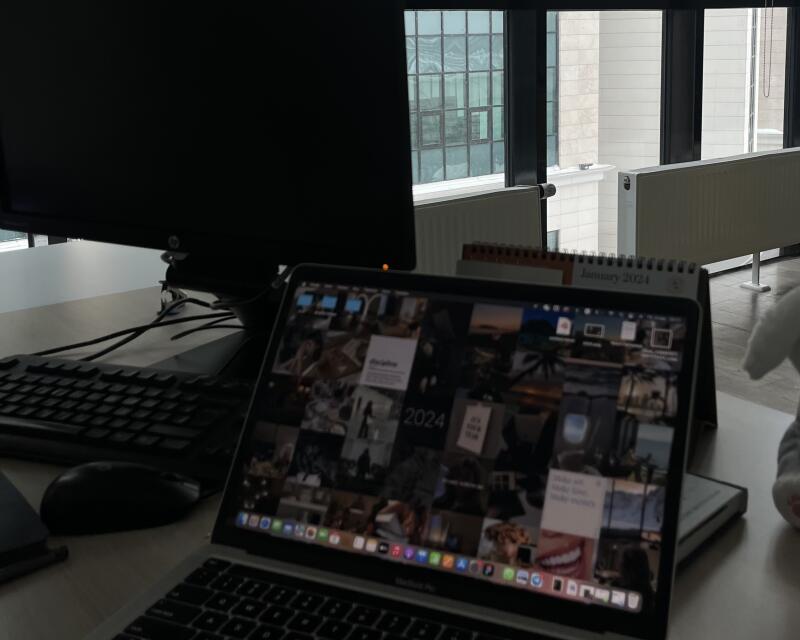 A desk with a laptop showing a collage of images as its background, a keyboard, a mouse, a monitor, and a January 2024 calendar.