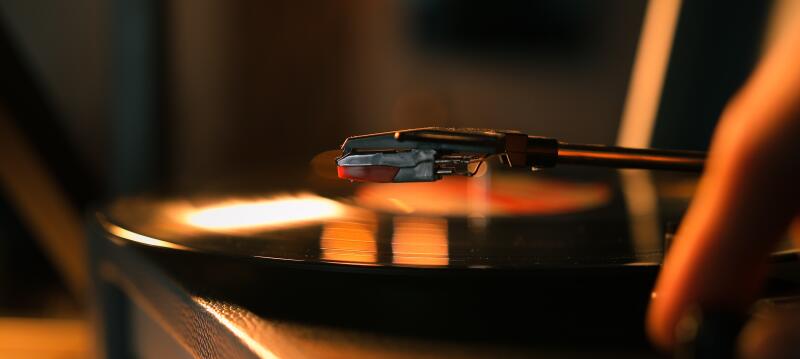 A record player needle rests on a spinning vinyl record, with a blurry hand nearby.