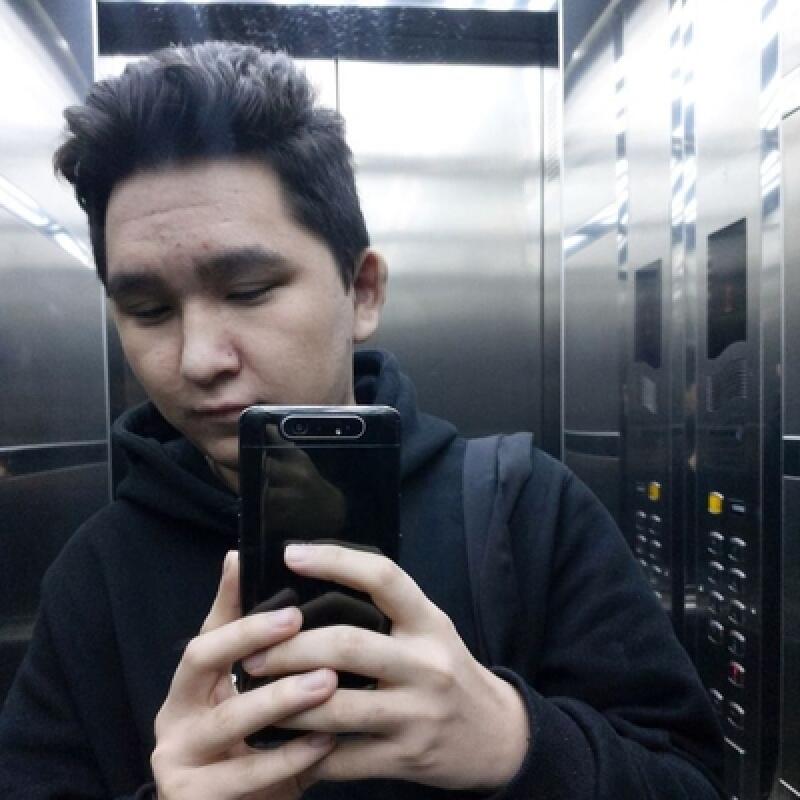 A man in a black hoodie takes a selfie in an elevator, holding a black smartphone.