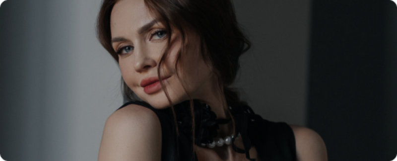 A portrait of a woman with blue eyes and brown hair, wearing a black top with a pearl necklace.