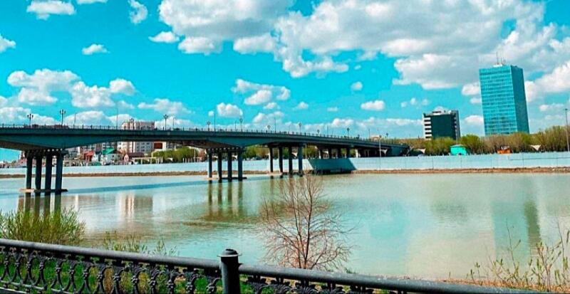The image shows a bridge over a river with buildings in the background under a partly cloudy sky.
