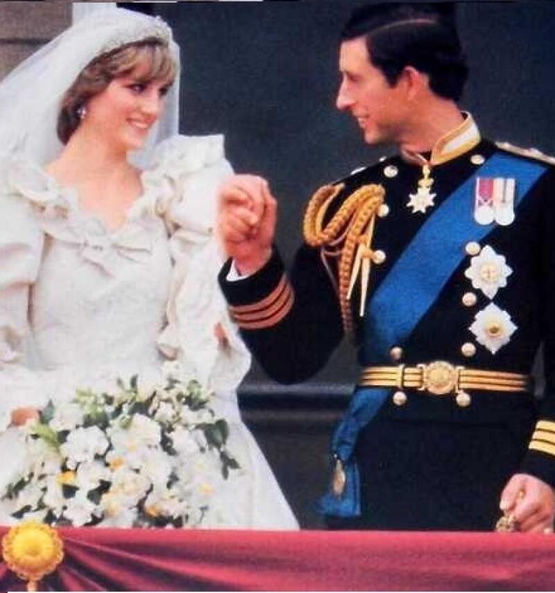 A photo of Prince Charles and Princess Diana on their wedding day, with Diana in a white wedding dress and veil, holding a bouquet of flowers, and Charles in a black military uniform with gold accents and a blue sash, holding hands.