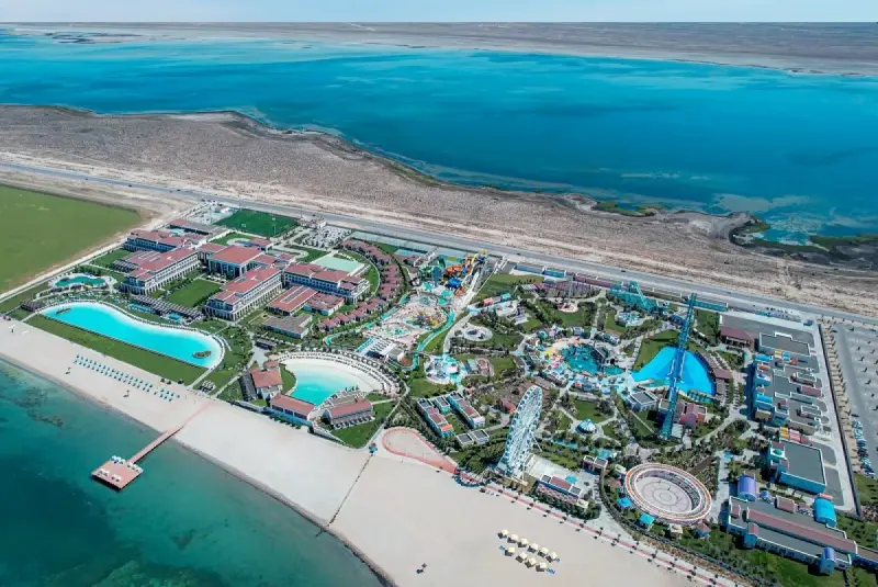 Aerial view of a large resort complex with hotels, water parks, pools, and a Ferris wheel near the coastline.