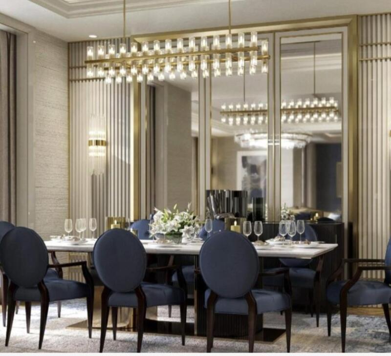 A dining room with a white marble table surrounded by eight blue chairs, a gold chandelier, and mirrored walls.