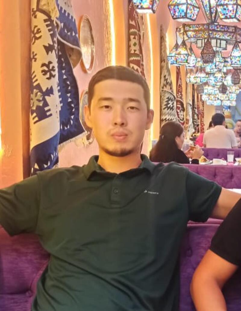 A man in a green polo shirt is sitting on a purple sofa in a room decorated with colorful lamps and patterned tapestries.