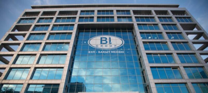 A multi-story office building with blue glass windows features the 'BI Group' logo and the text 'БҰЛ - БАҚЫТ МЕКЕНІ'.