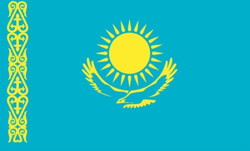 The image shows the flag of Kazakhstan, which features a golden sun with 32 rays above a golden steppe eagle, both centered, with a national ornamental pattern vertically on the left side, all on a light blue background.