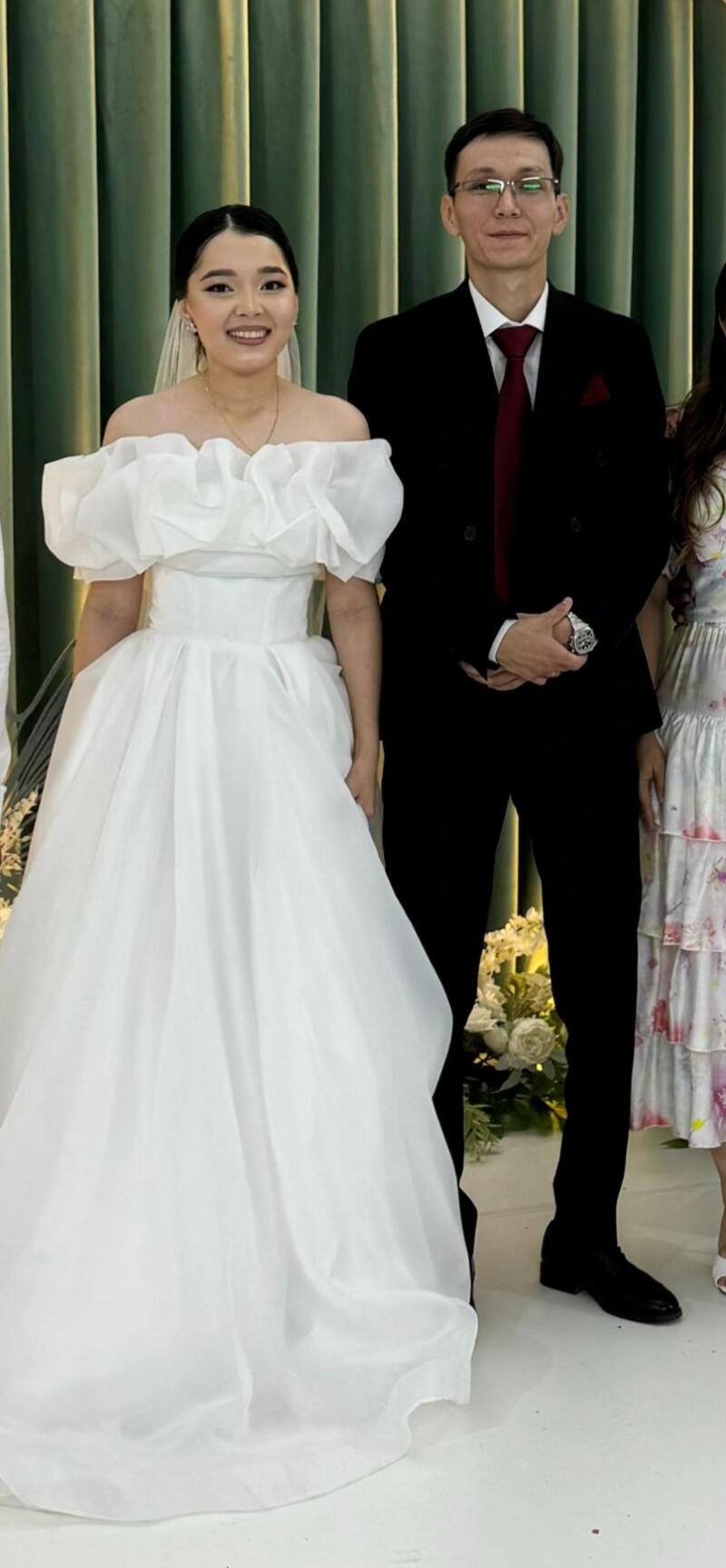 A bride in a white dress stands next to a man in a black suit with a red tie.