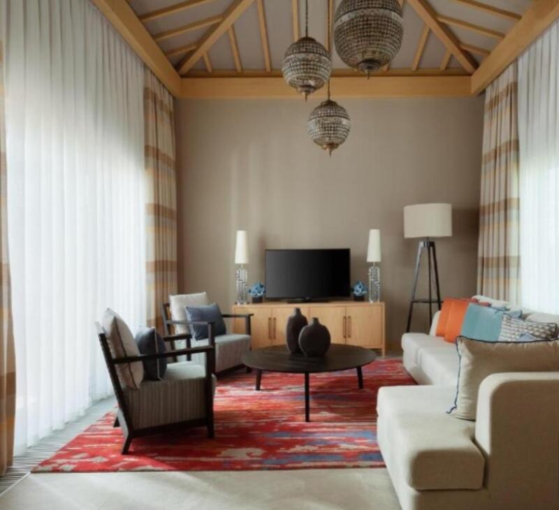 The living room features a sofa, chairs, a TV, and a red patterned rug, illuminated by three hanging lights.