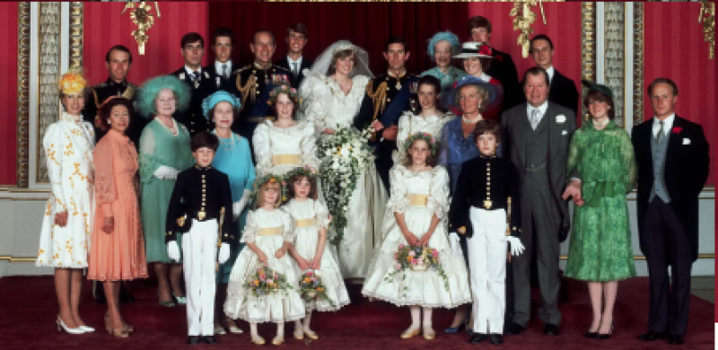 A full shot of the wedding of Prince Charles and Princess Diana with the wedding party standing in formal attire, including the bride in a large white gown and veil, and the groom in military dress.