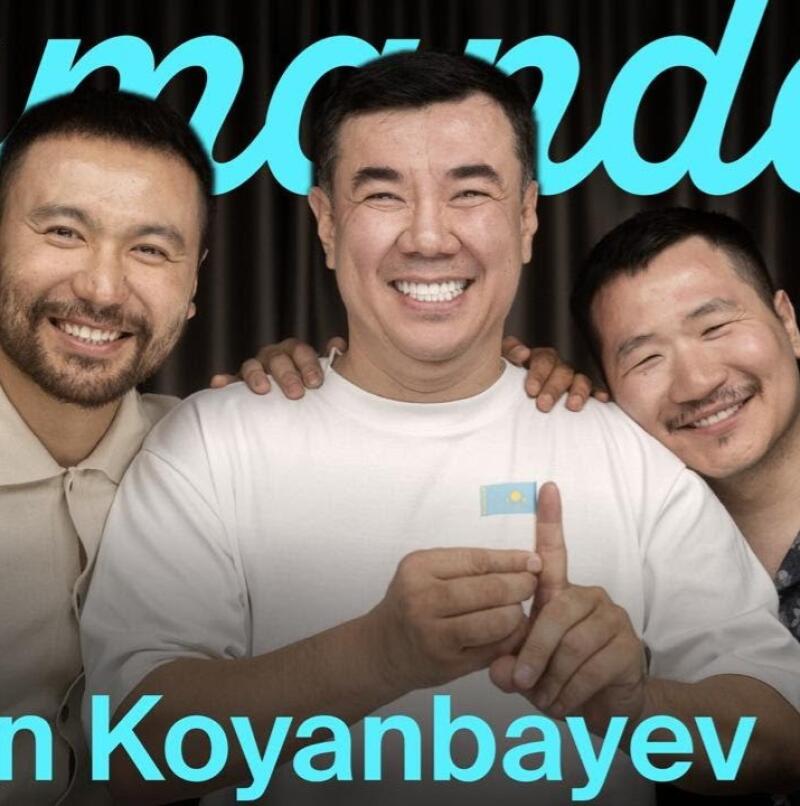 Three smiling men pose together; the man in the center holds a small Kazakhstan flag, and the image includes the text "n Koyanbayev" and a stylized word in turquoise above them.