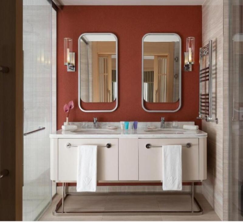 The image shows a bathroom with a double sink vanity, two mirrors, and a red wall. Each sink has a white towel hanging from the cabinet.