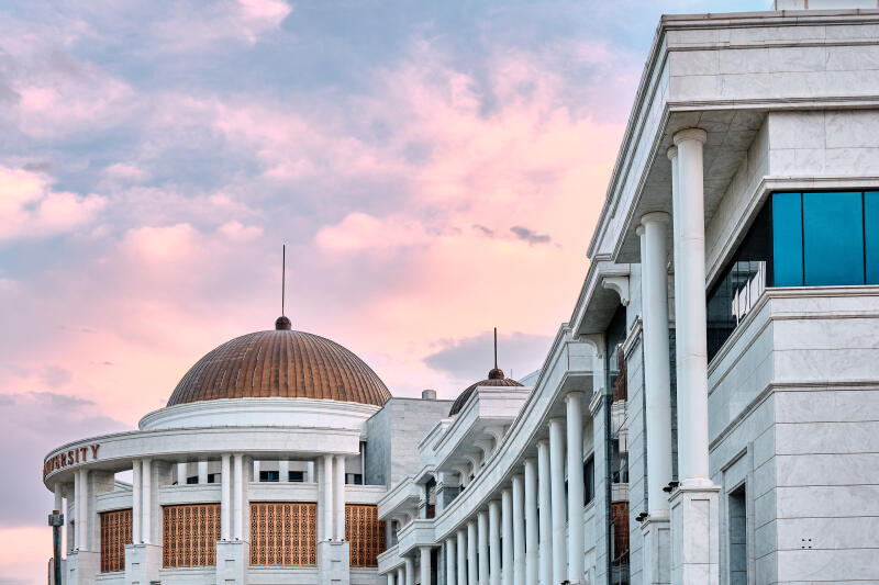 The image shows a white stone building with a dome and columns under a pink and blue sky, with the word "University" visible on the building.