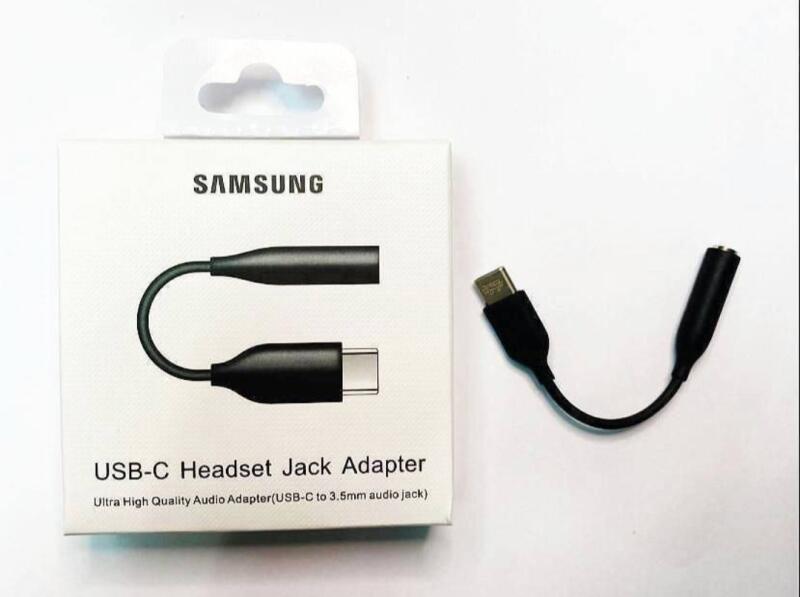 На изображении представлен адаптер разъема для гарнитуры Samsung USB-C рядом с его упаковкой, на которой написано "USB-C Headset Jack Adapter, Ultra High Quality Audio Adapter (USB-C to 3.5mm audio jack)".