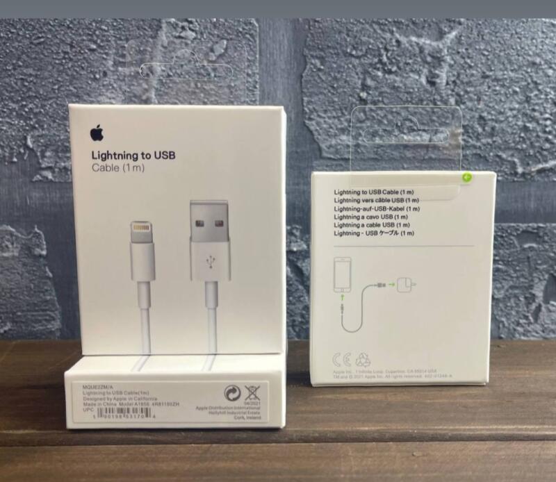 Две белые коробки кабеля Apple Lightning to USB (1 м) стоят на деревянной поверхности на сером фоне.