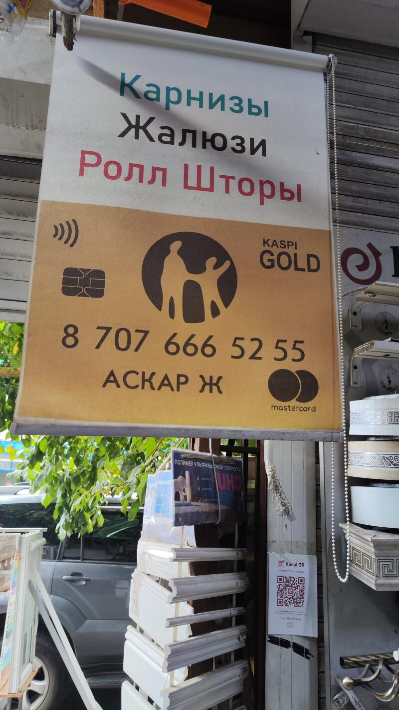 The image shows an advertisement banner for curtains, blinds, and roller blinds, designed like a Kaspi Gold card with the phone number 8 707 666 52 55, and the name Askar Zh.