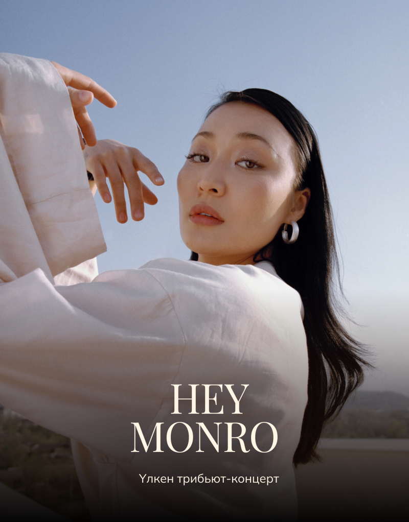 A woman with dark hair and fair skin is looking at the camera wearing a white top and silver hoop earrings; the text "HEY MONRO Улкен трибьют-концерт" is displayed on the bottom of the image.