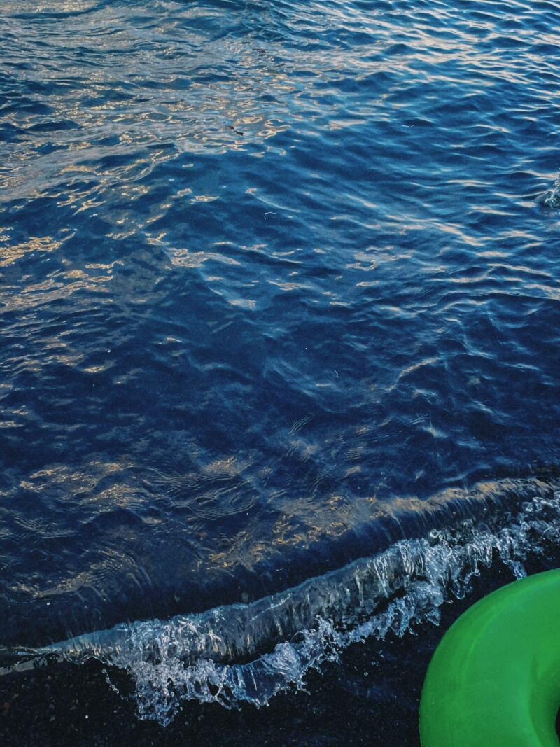 The image features dark blue water with small waves lapping onto a dark shore, and a portion of a green inflatable tube is visible in the lower right corner.