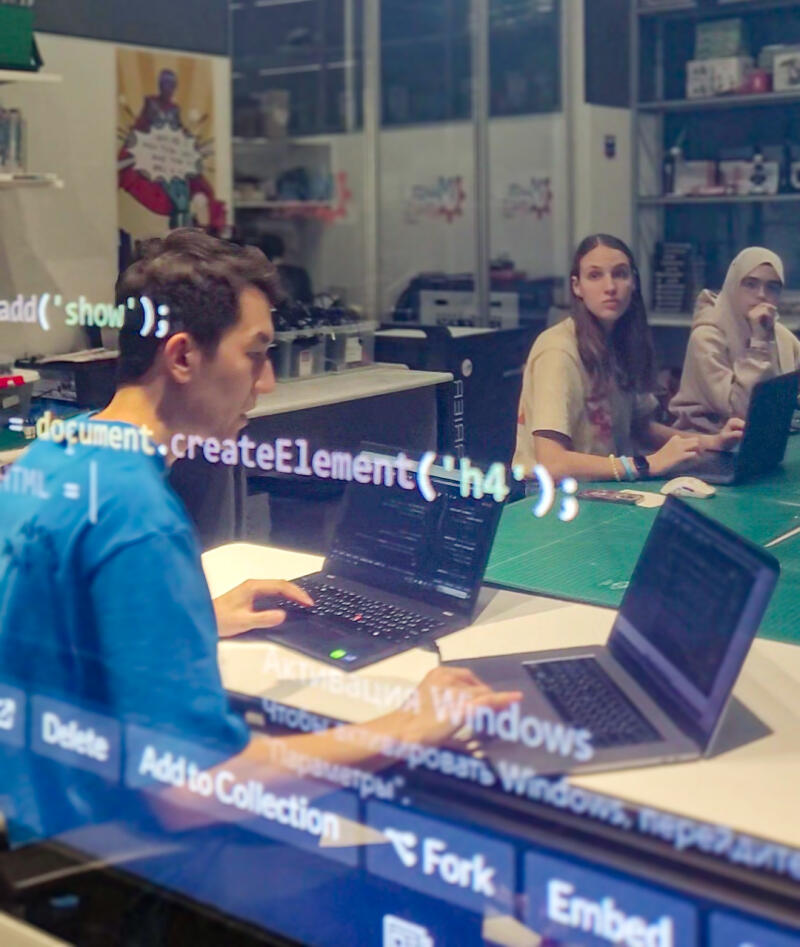The photo shows three people working on laptops at a table, with code visible on a screen in the foreground, including the text 'add('show');', '=document.createElement('h4');', 'HTML =', 'Активация Windows', and options like 'Delete', 'Add to Collection', 'Fork', and 'Embed'.
