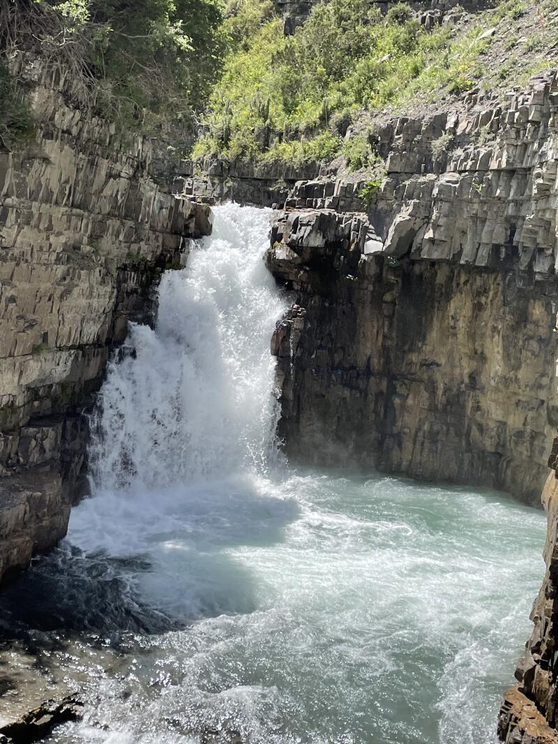 A waterfall cascades into a pool of water, surrounded by rocky cliffs and greenery.