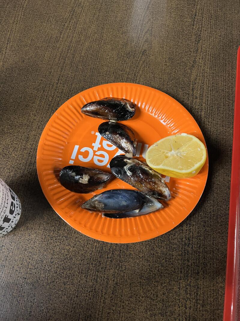 On an orange plate are five mussels and a lemon wedge.