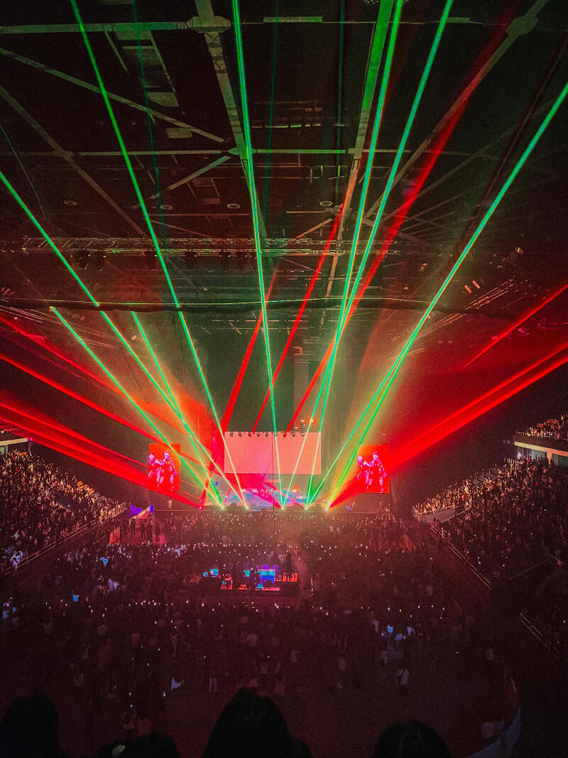A concert crowd with red and green laser lights illuminating the stage and the audience.