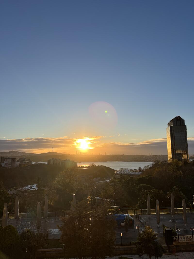 The image shows a city skyline at sunset with a body of water in the background and a tall modern building on the right.