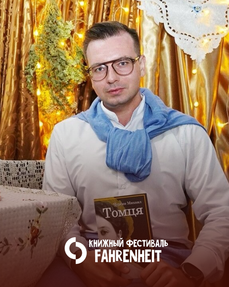 Мужчина в очках, белой рубашке и синем свитере, наброшенном на плечи, держит книгу с названием «Томця». В нижней правой части изображения расположен белый логотип и текст «КНИЖНЫЙ ФЕСТИВАЛЬ FAHRENHEIT», фон состоит из золотых штор с гирляндами и зеленью.