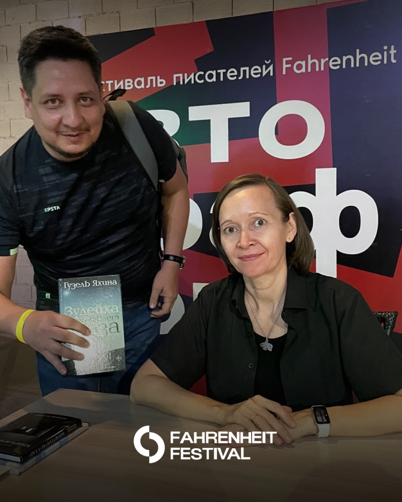 Мужчина держит книгу Гузель Яхиной под названием «Зулейха открывает глаза» рядом с автором на фоне баннера фестиваля «Фаренгейт».