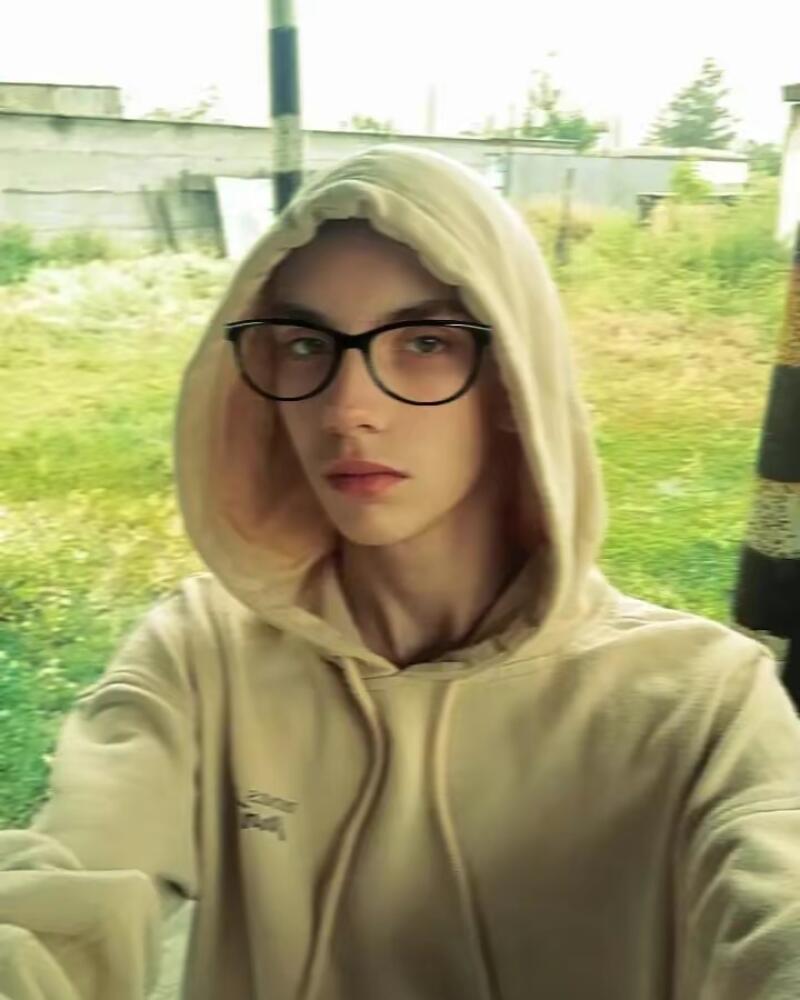 A person with glasses and a beige hoodie stands outside.