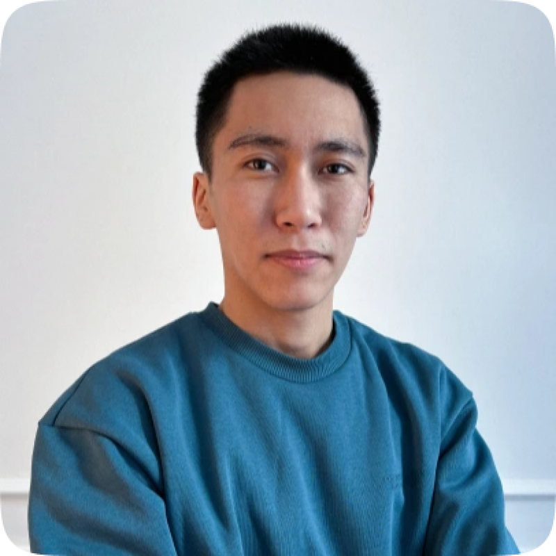 A young man with short black hair is wearing a teal sweater and looking at the camera against a plain white background.