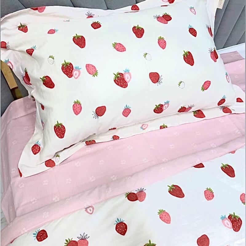 A close-up shows a pillow and sheets with a strawberry pattern, with a pink sheet visible beneath the strawberry-themed bedding.