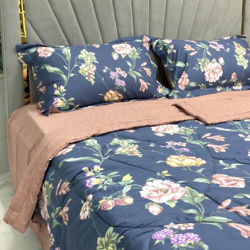 The image shows a bed with a floral patterned comforter and pillows, with a light pink sheet set. The headboard is gray and tufted.