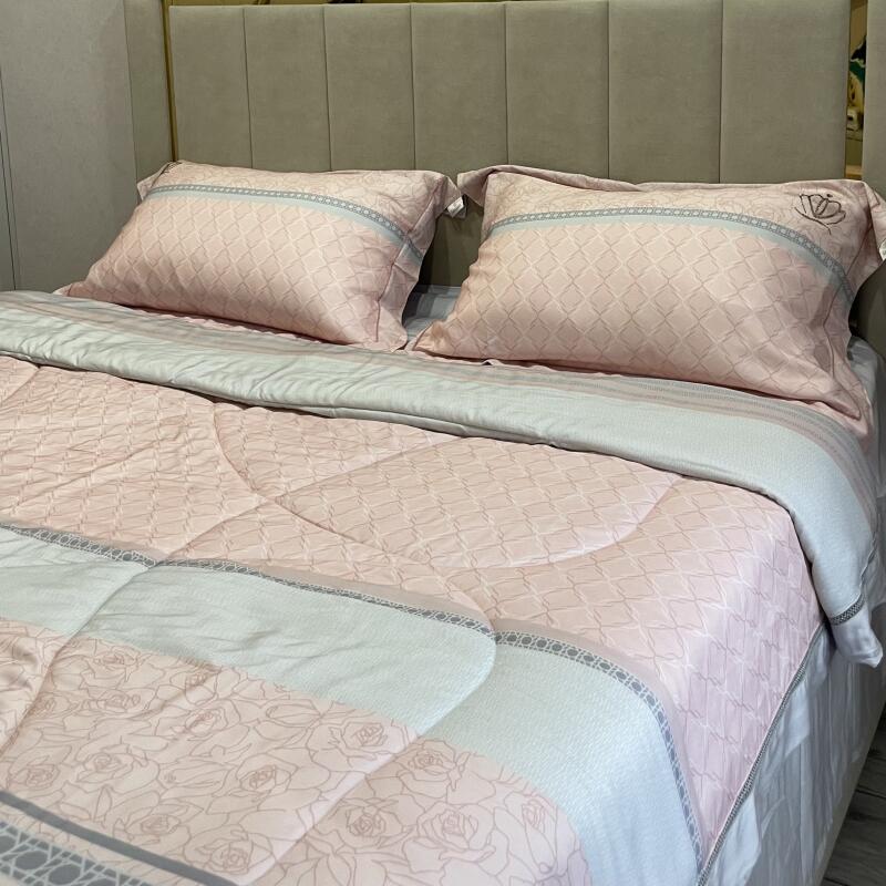 A bed with two pillows and a comforter, all in shades of pink and white with geometric and floral patterns, set against a beige headboard.