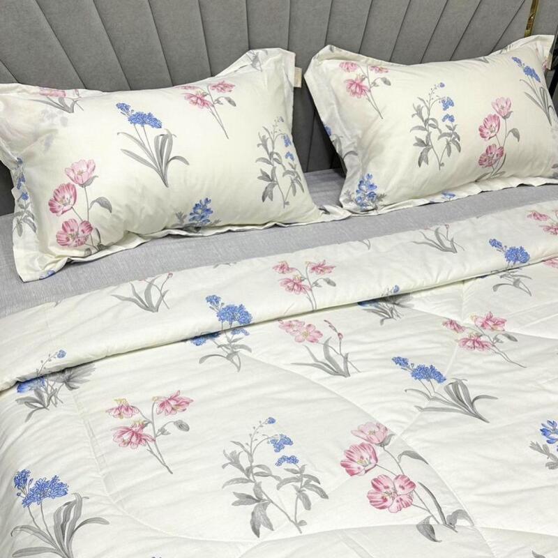 The image shows a bed with two pillows and a comforter, all with a floral pattern in pink and blue on a white background.