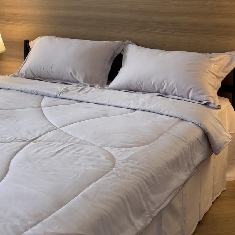 A bed with a light gray comforter and two pillows is set against a wooden headboard.
