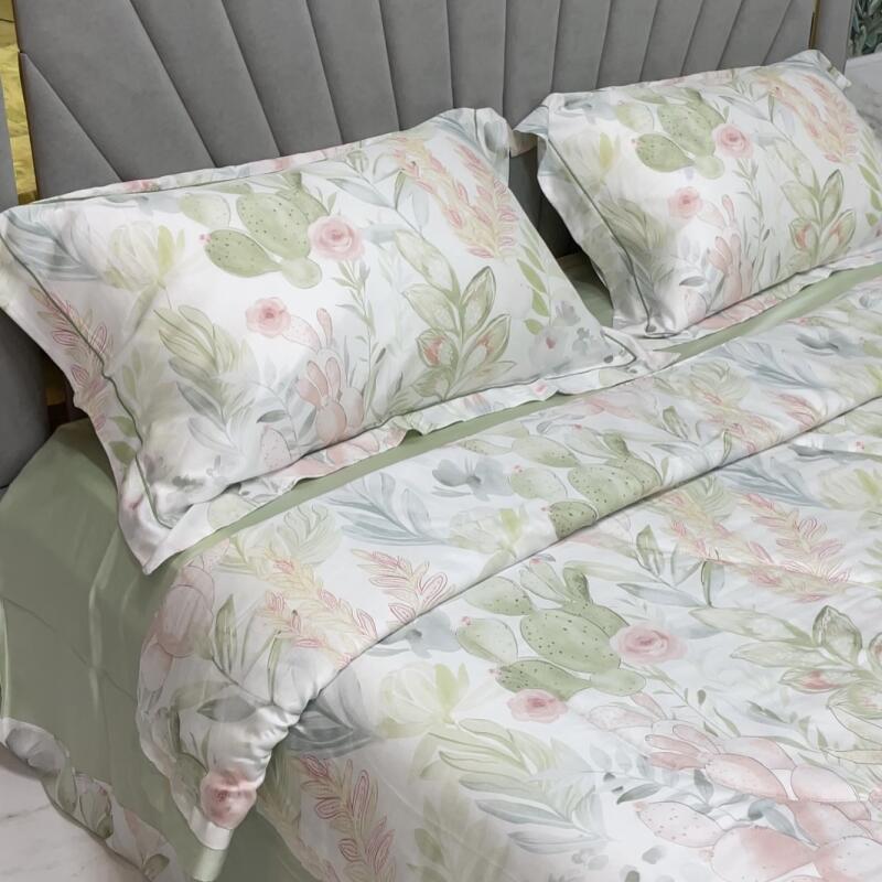 The image shows a bed with floral-patterned bedding, including two pillows, featuring cacti and roses on a white background, and a light green sheet.