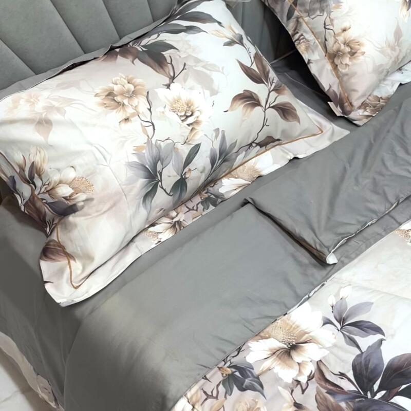 A bed is neatly made with a gray comforter, and floral patterned pillows and duvet.