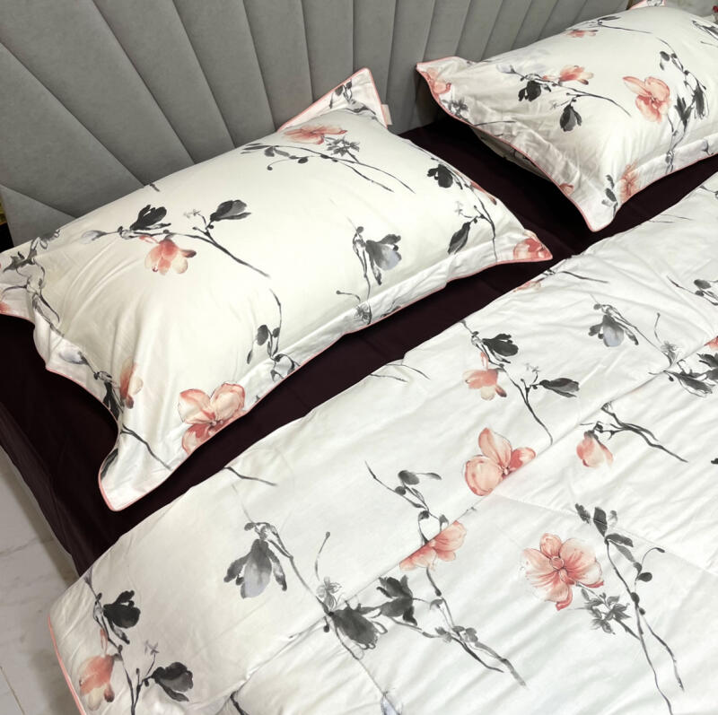 The image shows a set of floral-patterned bedding with a white background, featuring pale pink and gray flowers and branches. The set includes two pillows and a comforter, all with a pink trim.