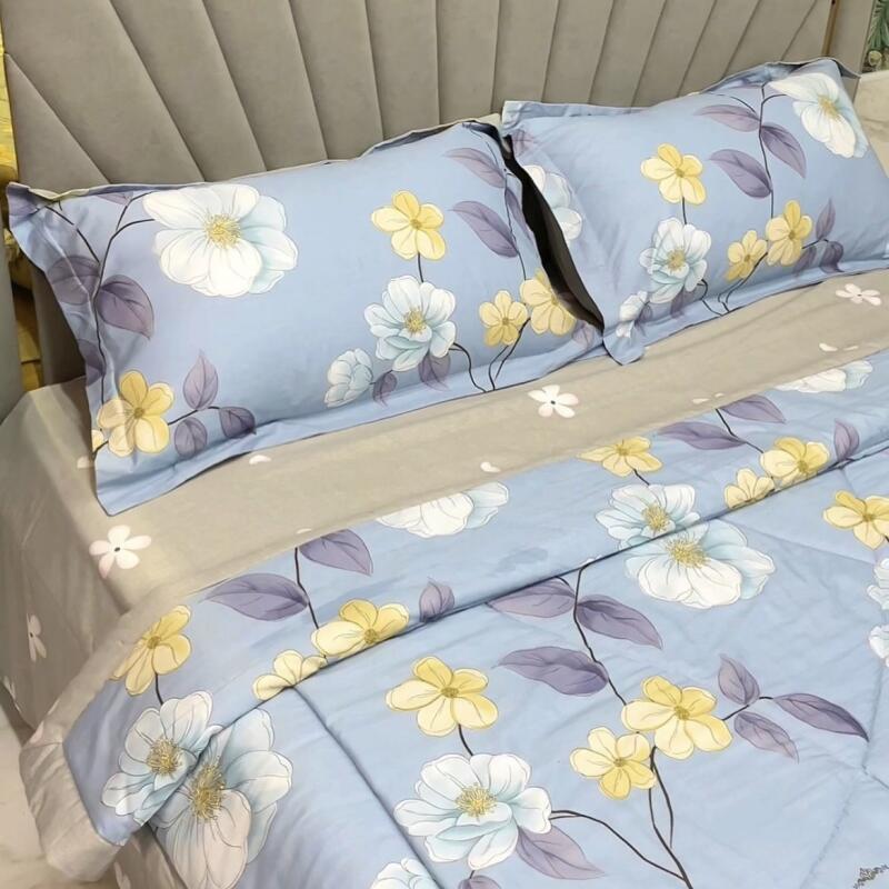 The image shows a bed with blue floral-patterned bedding and two pillows with the same pattern. The floral design features white and yellow flowers with purple leaves.