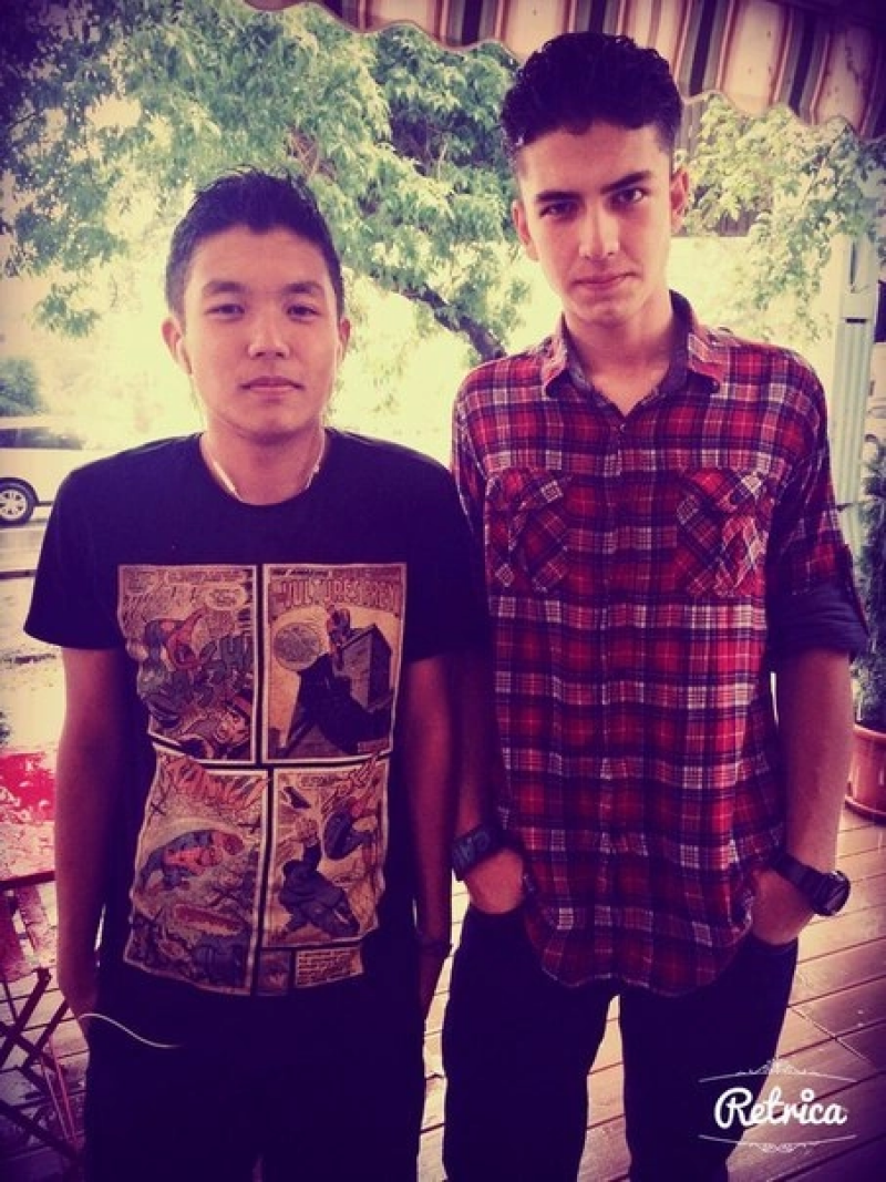 Two men are standing next to each other; one is wearing a comic book t-shirt, and the other is wearing a red and black plaid shirt.