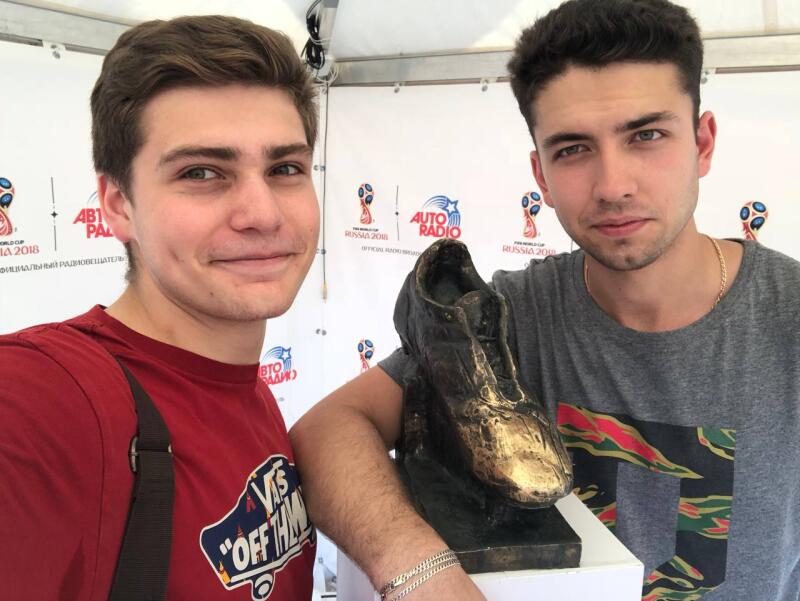 Two young men pose with a gold-colored shoe statue in front of a backdrop that reads "AUTO RADIO RUSSIA 2018."