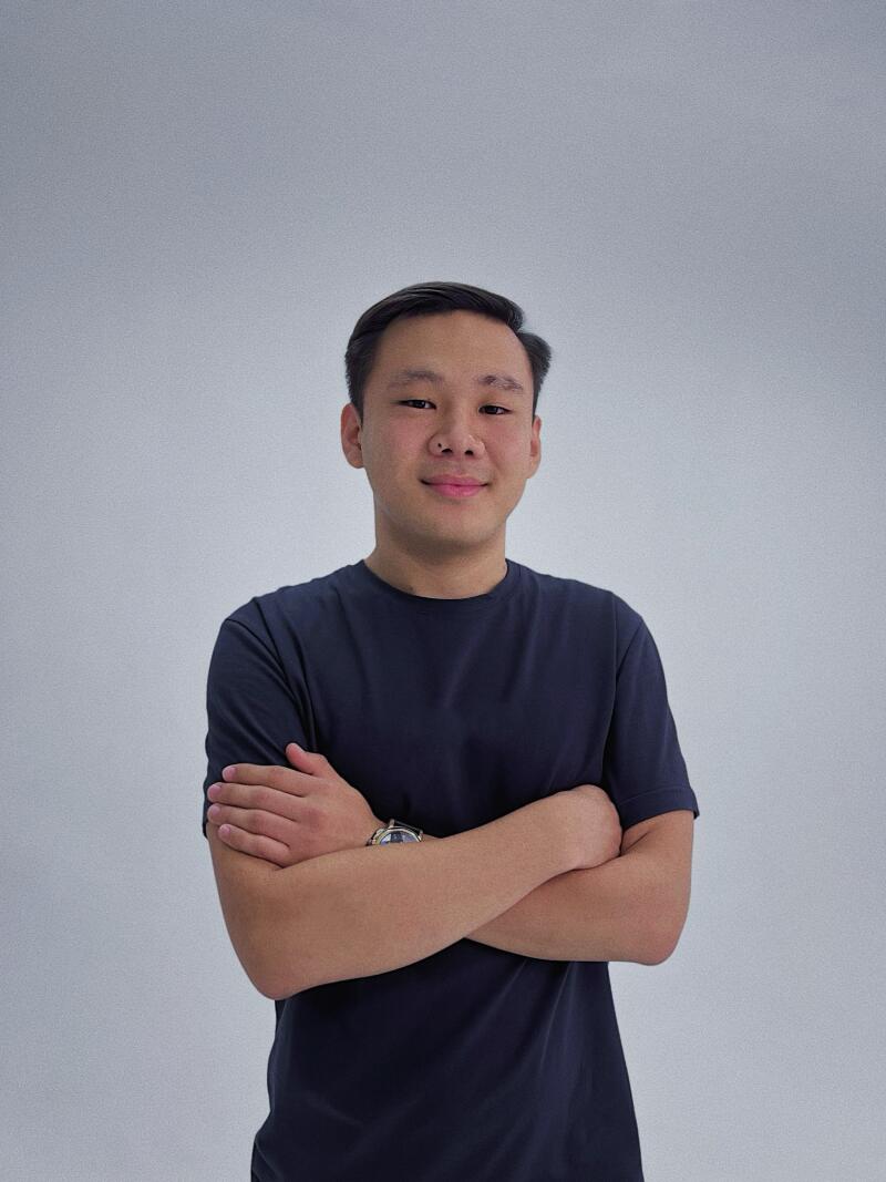 A man with a nose piercing is wearing a dark blue T-shirt and has his arms crossed.
