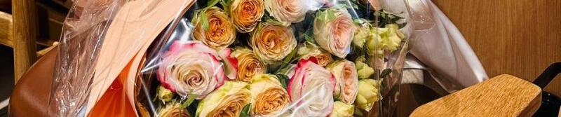 A bouquet of roses is wrapped in clear cellophane and peach-colored paper.