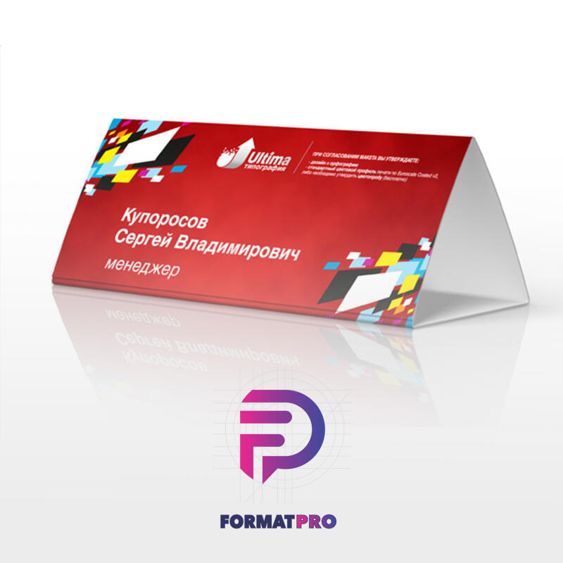 A triangular table tent card with a red background displays the name "Купоросов Сергей Владимирович," the job title "менеджер," and the logo of "Ultima типография." Colorful geometric shapes adorn the top and right sides of the card, and some small text is visible in the upper right corner.