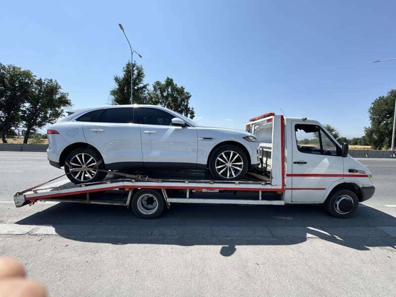 A white Jaguar SUV is secured on a white tow truck with red accents on a sunny day.